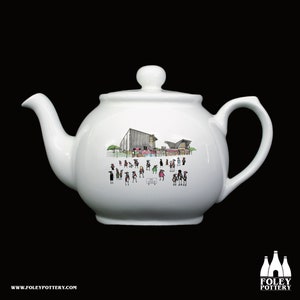 May include: White ceramic teapot featuring a black and white illustration of a building and people. The text "The Stoop" is printed on the teapot.