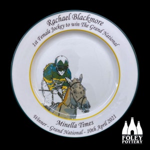 May include: A white ceramic plate with a green and gold rim, featuring a hand-drawn illustration of a jockey on a horse. Text on the plate reads "Rachael Blackmore, 1st Female Jockey to win The Grand National" and "Minella Times, Winner - Grand National - 10th April 2021."
