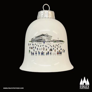May include: White ceramic Christmas bauble shaped like a bell with a silver top. The bauble features a black and white illustration of a stadium with a crowd of people in front of it. The text "AZ Bell Stadium" is visible on a sign in the illustration.