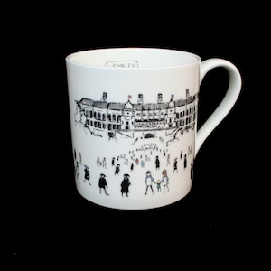 May include: White ceramic mug with a black and white illustration of Wembley Stadium and people walking around it. The text "Wembley" is printed on the mug.