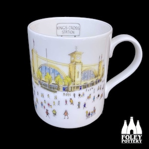 Può includere: Tazza in ceramica bianca con un'illustrazione colorata della stazione di King's Cross a Londra. La tazza ha un manico nero e il testo "Kings Cross Station" è stampato sul davanti.