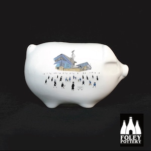May include: White ceramic piggy bank with a black and white illustration of a stadium and people. The text "FOOTBALL GROUND" is on a sign in the illustration. The piggy bank is made by Foley Pottery.