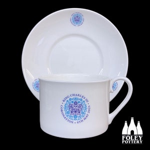 May include: White teacup and saucer with a blue and purple design featuring a crown and the text "KING CHARLES III CORONATION 6TH MAY 2023".