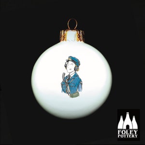 May include: White Christmas bauble with a hand-painted illustration of a woman wearing a blue uniform and a headset. The bauble is decorated with gold trim and features the text "FOLEY POTTERY".