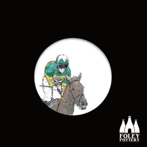 May include: A white ceramic round button featuring a black and white illustration of a jockey riding a horse. The jockey is wearing a green and yellow racing suit and a white helmet. The horse is brown and has a black bridle.