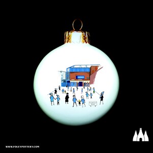 Può includere: Palloncino di Natale bianco con un'illustrazione blu e rossa di uno stadio e persone che camminano verso di esso. Il testo "HIGHFIELD ROAD" è visibile sul palloncino.