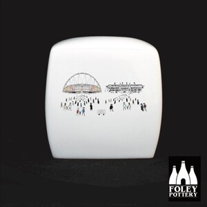 May include: White ceramic sugar jar with a black and white illustration of a stadium and a crowd of people. The illustration includes the text "Wembley Stadium". The jar is made by Foley Pottery.