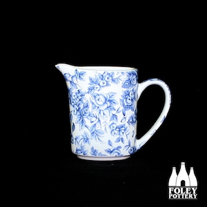 May include: A white ceramic pitcher with a blue floral pattern. The pitcher has a handle and a spout.