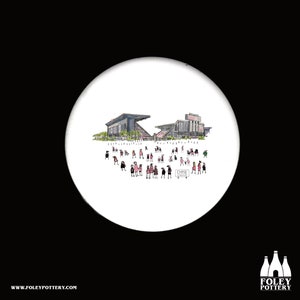 May include: A white ceramic coaster with a hand-drawn illustration of a football stadium with people in the foreground. The stadium is black and white, and the people are wearing pink and white. The text "CHASE FIELD" is visible on a sign in the foreground.