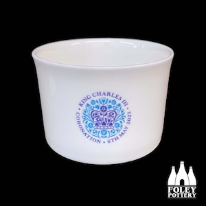 May include: White ceramic mug with a blue and purple design commemorating King Charles III's coronation on May 6th, 2023. The design features a crown, flowers, and the text "King Charles III Coronation 6th May 2023".