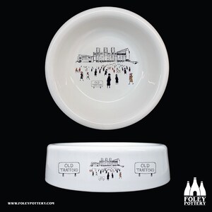 May include: White ceramic dog bowl with a black and white illustration of Old Trafford football stadium and fans. The bowl has the words "Old Trafford" printed on it.