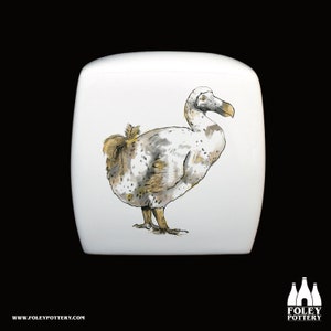 May include: White ceramic box with a hand-painted illustration of a dodo bird. The dodo is depicted in a realistic style with brown and gray feathers.
