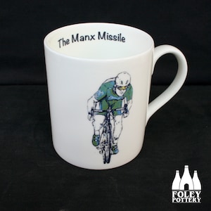 May include: White ceramic mug with a black and white illustration of a cyclist on a bicycle. The text "The Manx Missile" is printed on the top of the mug.