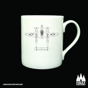 May include: White ceramic mug with a black line drawing of a P-38 Lightning fighter plane. The plane is facing upwards with the wings spread out. The plane has a red, white, and blue star on each wing.