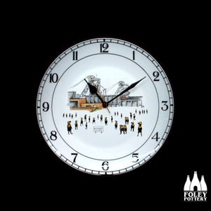 May include: A white ceramic clock with black numbers and hands. The clock face features a black and white illustration of a coal mine with a sign that reads "Bustyore Colliery".
