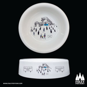 May include: White ceramic dog bowl with a black and white illustration of a stadium and people walking towards it. The illustration includes the text "Selhurst Park".