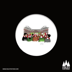 May include: A white ceramic coaster with a hand-drawn illustration of a crowd of people wearing red and white scarves and hats, watching a soccer game in a stadium.