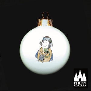 May include: White Christmas bauble featuring a cartoon illustration of a pilot wearing a headset and goggles. The bauble is decorated with a gold top.