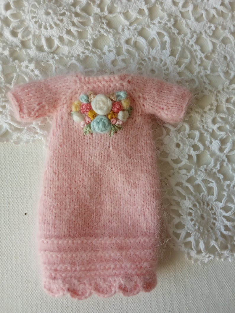 Puede incluir: Un vestido de beb&eacute; de punto rosa con un dise&ntilde;o de bordado floral en la parte delantera.