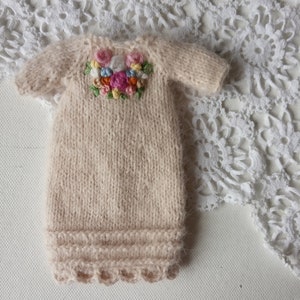 Puede incluir: Un vestido de beb&eacute; de punto beige con un dise&ntilde;o de bordado floral en el escote.
