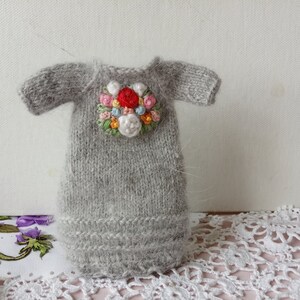 Puede incluir: Un vestido de mu&ntilde;eca de punto gris con un dise&ntilde;o de bordado floral en tonos de rosa, rojo, blanco y azul.