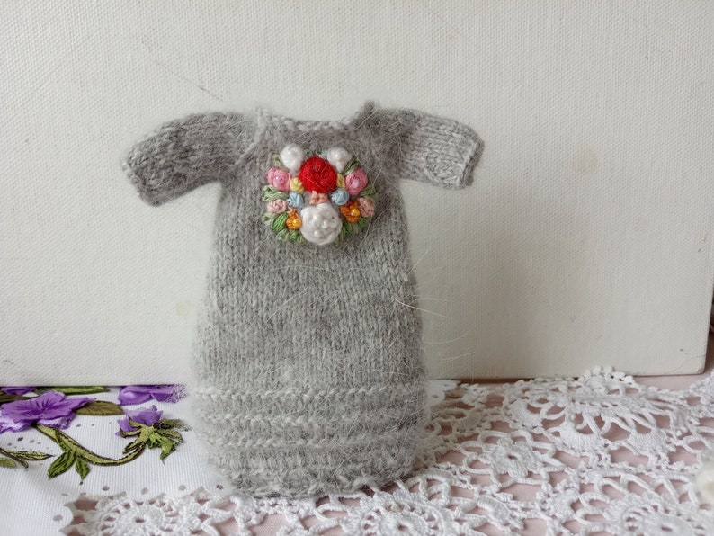 Puede incluir: Un vestido de mu&ntilde;eca de punto gris con un dise&ntilde;o de bordado floral en tonos de rosa, rojo, blanco y azul.