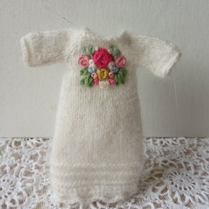 Puede incluir: Un vestido blanco de punto con un dise&ntilde;o de bordado floral en la parte delantera. El bordado presenta flores rosas, amarillas, azules y verdes.