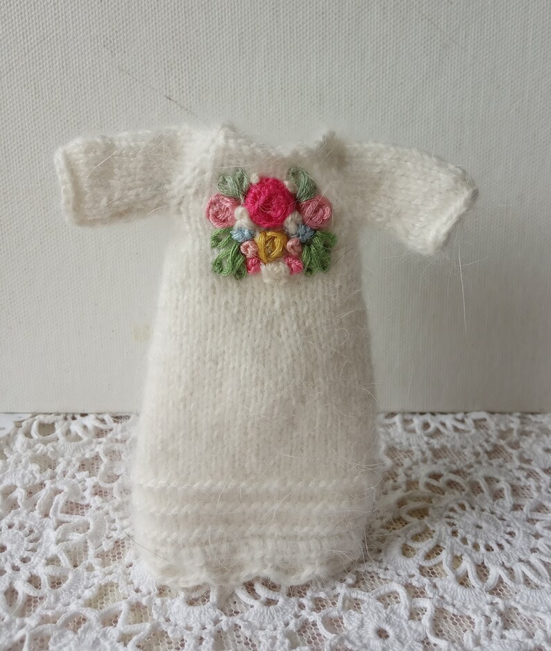 Puede incluir: Un vestido blanco de punto con un dise&ntilde;o de bordado floral en la parte delantera. El bordado presenta flores rosas, amarillas, azules y verdes.