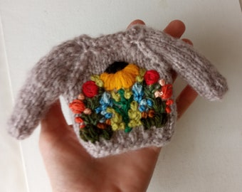 May include: A gray knitted sweater with a colorful embroidered floral design featuring a yellow sunflower, red, orange, and blue flowers, and green leaves.