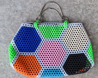 Pode incluir: Uma pequena bolsa de mão de contas coloridas com uma alça de prata. A bolsa é feita de contas hexagonais em tons de azul, verde, rosa, laranja, branco e preto.