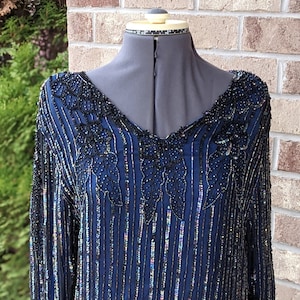 May include: A navy blue sequined dress with black beading in a floral pattern. The dress has long sleeves and a V-neckline.