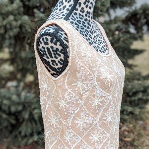 May include: A sleeveless sequined top with a delicate floral pattern in white sequins on a pale pink background.