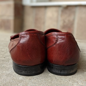 Pode incluir: Um par de mocassins de couro marrom com solas pretas. Os mocassins s&atilde;o usados e t&ecirc;m um aspecto envelhecido.