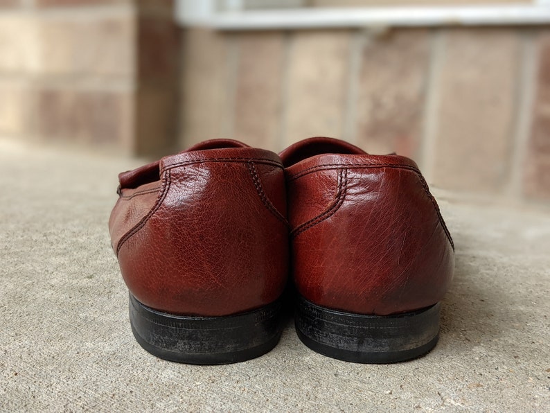 Pode incluir: Um par de mocassins de couro marrom com solas pretas. Os mocassins s&atilde;o usados e t&ecirc;m um aspecto envelhecido.