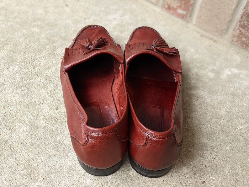 Pode incluir: Um par de mocassins de couro marrom com franjas e sola marrom escura. Os mocassins t&ecirc;m bico fino e um detalhe de franjas na parte superior.