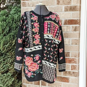 May include: A black cardigan sweater with a floral and geometric pattern. The cardigan has a button-up front and long sleeves.