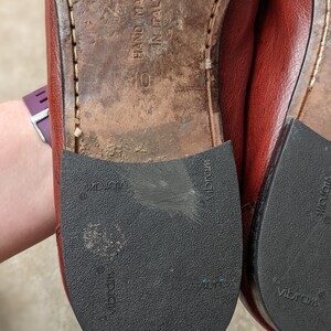 Pode incluir: Close-up da parte inferior de um par de sapatos de couro marrom com solas pretas. As solas s&atilde;o etiquetadas com "Vibram" e "Hand Made in Italy".