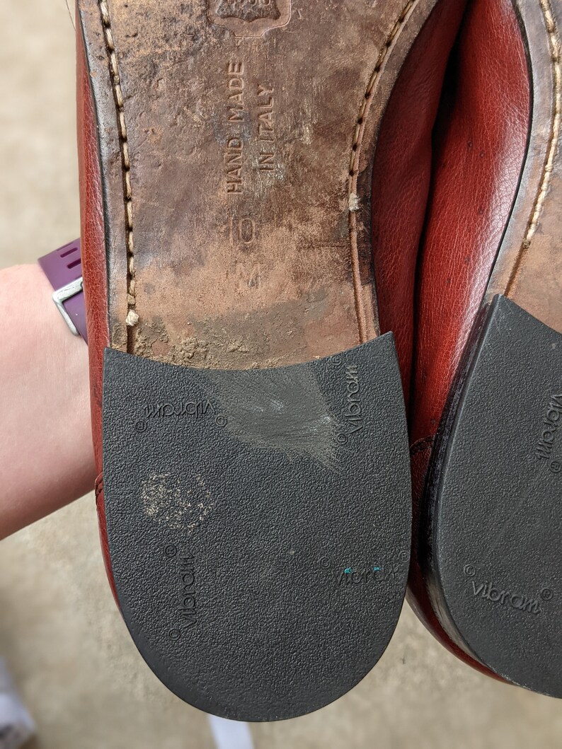 Pode incluir: Close-up da parte inferior de um par de sapatos de couro marrom com solas pretas. As solas s&atilde;o etiquetadas com "Vibram" e "Hand Made in Italy".
