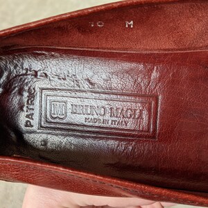 Pode incluir: Close-up do interior de um sapato de couro marrom com o texto "Bruno Magli Made in Italy" gravado na palmilha.