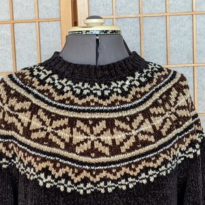 Op de afbeelding: Een bruine trui met een wit, bruin en zwart fair isle-patroon rond de hals.