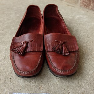 Pode incluir: Um par de mocassins de couro bord&ocirc; com franjas e uma borda costurada. Os mocassins s&atilde;o medidos com uma fita m&eacute;trica, mostrando um comprimento de 15,2 cm.