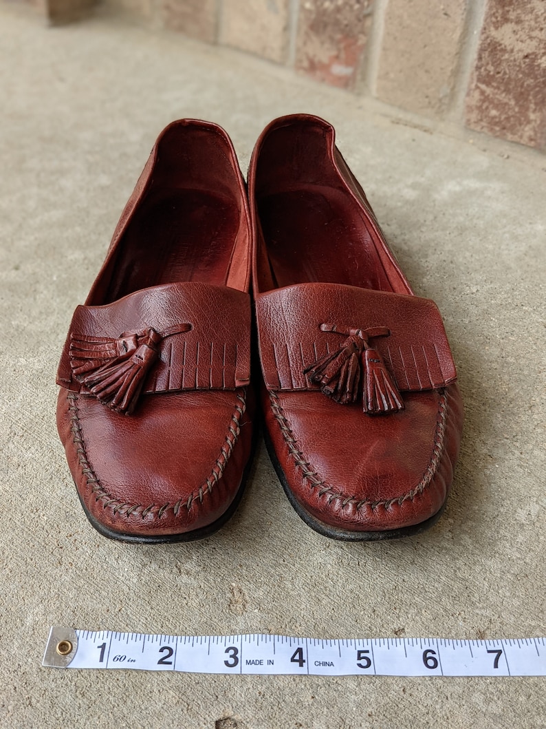 Pode incluir: Um par de mocassins de couro bord&ocirc; com franjas e uma borda costurada. Os mocassins s&atilde;o medidos com uma fita m&eacute;trica, mostrando um comprimento de 15,2 cm.
