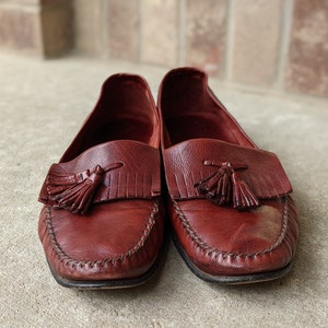 Pode incluir: Um par de mocassins de couro bord&ocirc; com borlas. Os mocassins t&ecirc;m uma borda costurada e uma ponta pontiaguda.