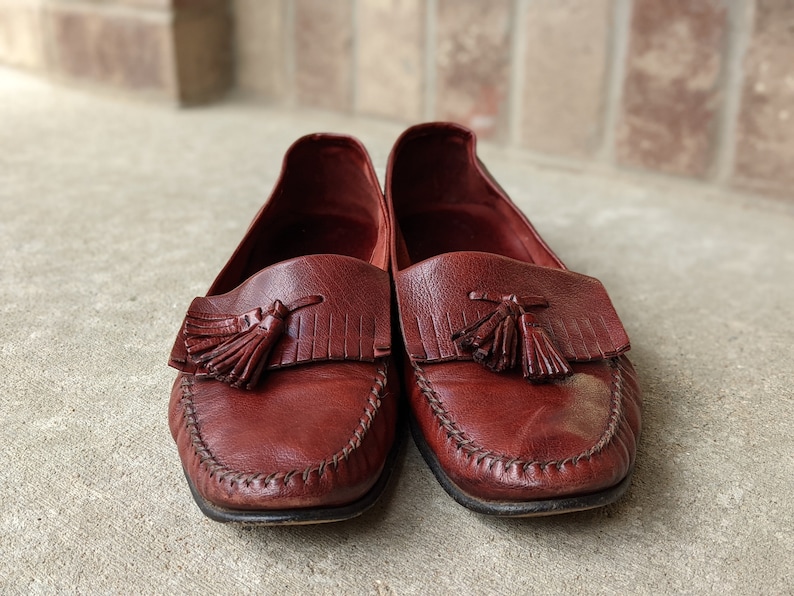 Pode incluir: Um par de mocassins de couro bord&ocirc; com borlas. Os mocassins t&ecirc;m uma borda costurada e uma ponta pontiaguda.