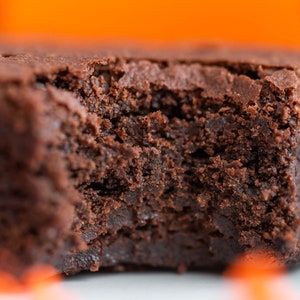 May include: A close-up of a chocolate brownie with a bite taken out of it. The brownie is dark brown and has a fudgy texture.