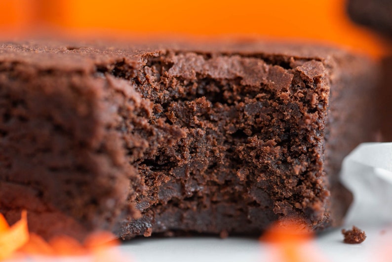 May include: A close-up of a chocolate brownie with a bite taken out of it. The brownie is dark brown and has a fudgy texture.