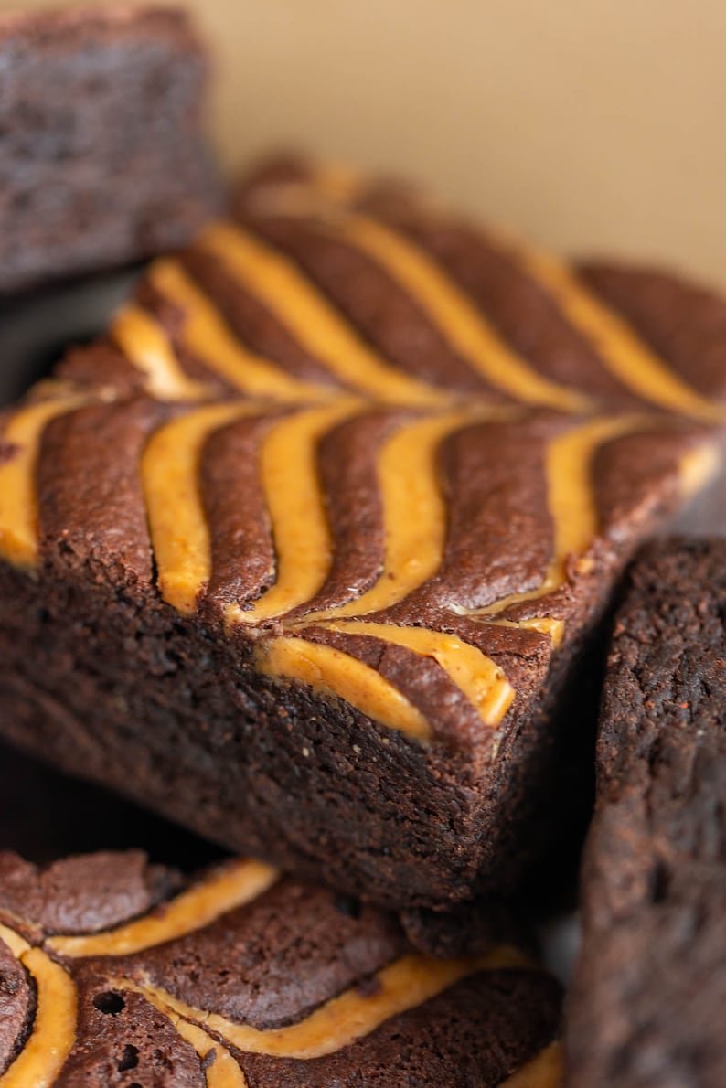 May include: Close-up of a stack of chocolate brownies with a swirl of peanut butter on top. The brownies are dark brown and the peanut butter is a light brown.