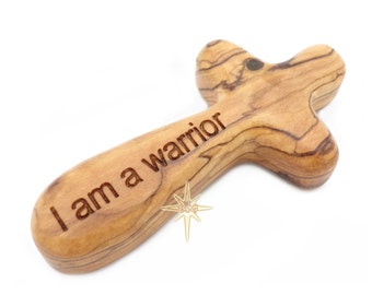May include: A wooden cross with the words "I am a warrior" engraved on it. The cross is made of olive wood and has a natural finish.