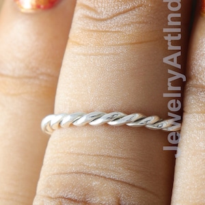 May include: A silver twisted band ring worn on a finger with orange nail polish.