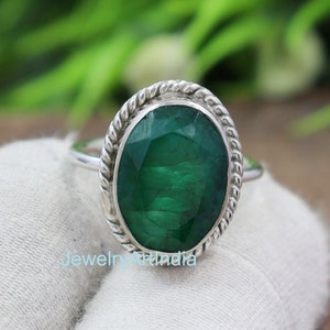 May include: A silver ring with a green oval emerald gemstone set in a rope-like band.